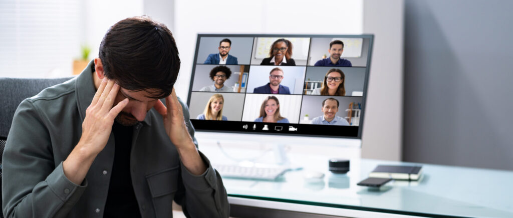 A man rubs his temples with a Zoom meeting in the background. Image credit: iStock