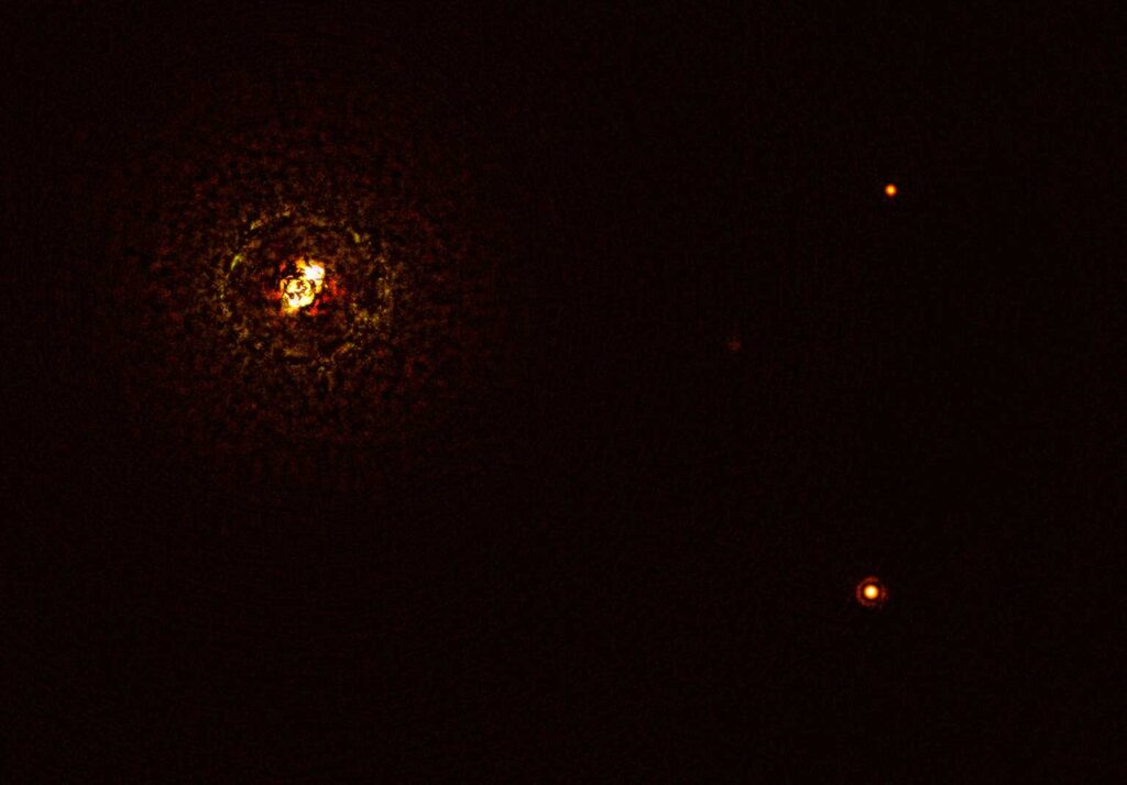This image shows the most massive planet-hosting star pair to date, b Centauri, and its giant planet b Centauri b. This is the first time astronomers have directly observed a planet orbiting a star pair this massive and hot. The star pair, which has a total mass of at least six times that of the sun, is the bright object in the top left corner of the image, the bright and dark rings around it being optical artefacts. The planet, visible as a bright dot in the lower right of the frame, is ten times as massive as Jupiter and orbits the pair at 100 times the distance Jupiter orbits the sun. The other bright dot in the image (top right) is a background star. By taking different images at different times, astronomers were able to distinguish the planet from the background stars. The image was captured by the SPHERE instrument on ESO’s Very Large Telescope and using a coronagraph, which blocked the light from the massive star system and allowed astronomers to detect the faint planet. Image credit: ESO/Janson et al.