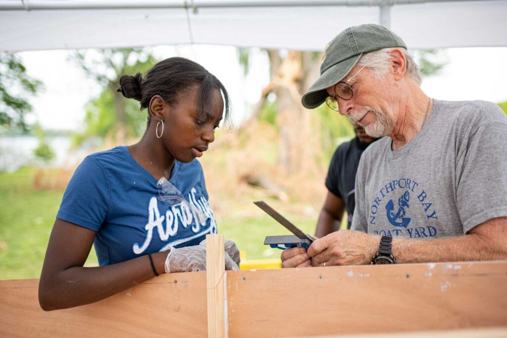 Strawberry Burrell (left), a resident of Detroit, and Detroit River Story Lab participant, works with a volunteer building a boat that the students will test in the Detroit River. Image credit: Eric Bronson, Michigan Photography