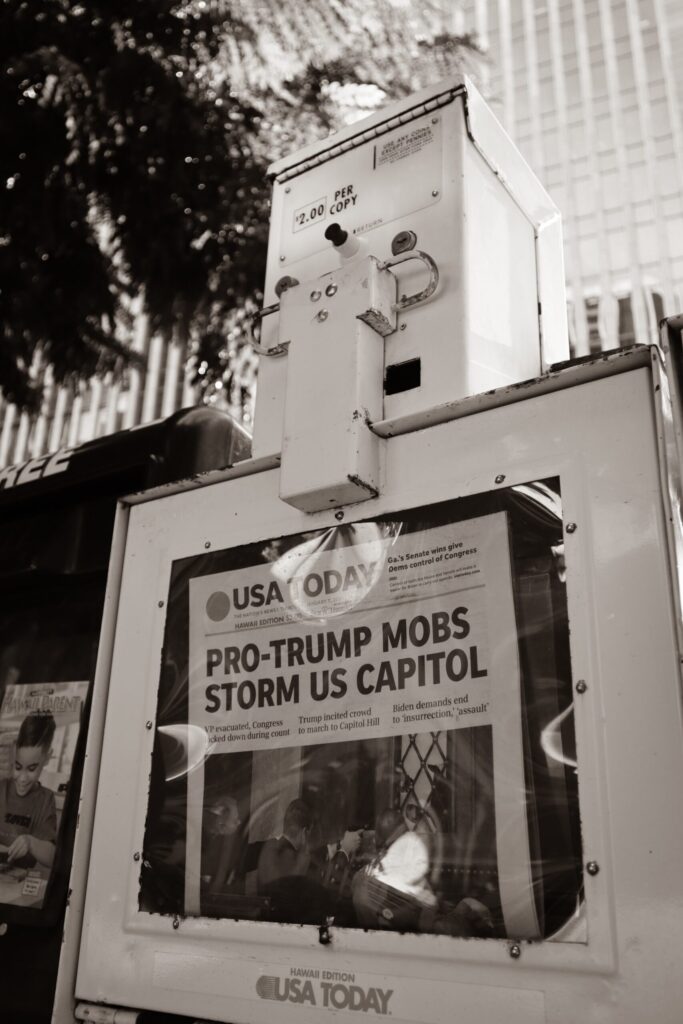 A newspaper rack showing a USA Today headline "Pro-Trump Mob Storms U.S. Capital". Image credit: @little_plant, Unsplash.com
