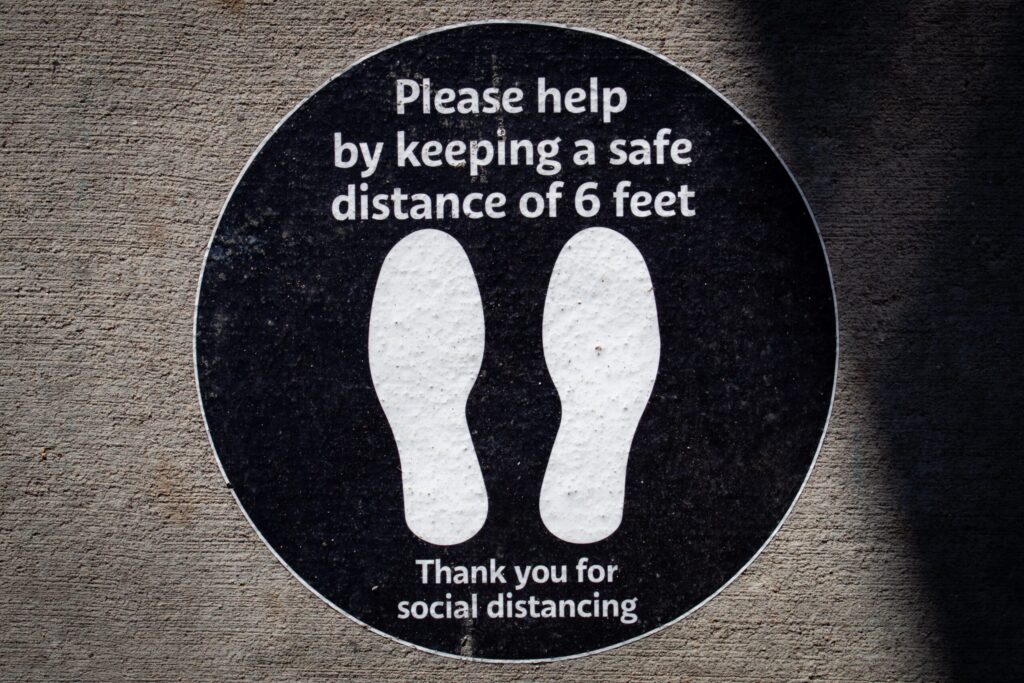 Floor sticker reading "Please help by keeping a safe distance of 6 feet." Image credit: Elizabeth McDaniel, Unsplash