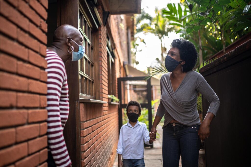 Daughter visiting mother at home during pandemic using surgical mask. Image credit: iStock