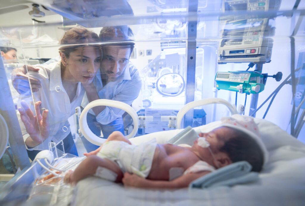 Worried young couple looking at their premature newborn in an incubator. Image credit: iStock