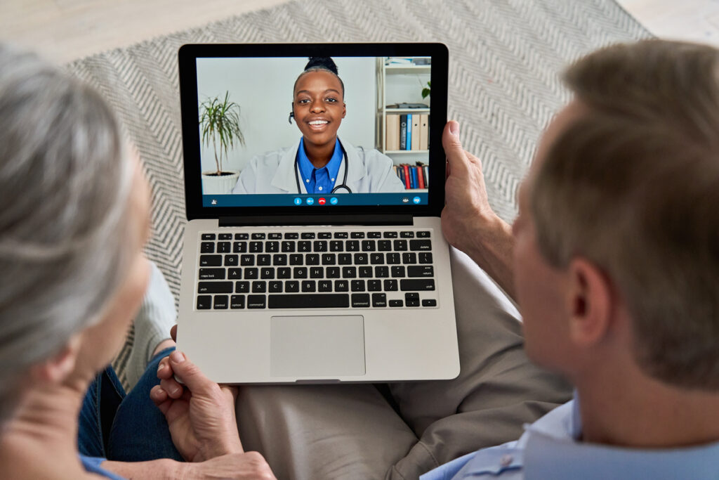 Over shoulder view of two people on a video call with a doctor. Image credit: iStock