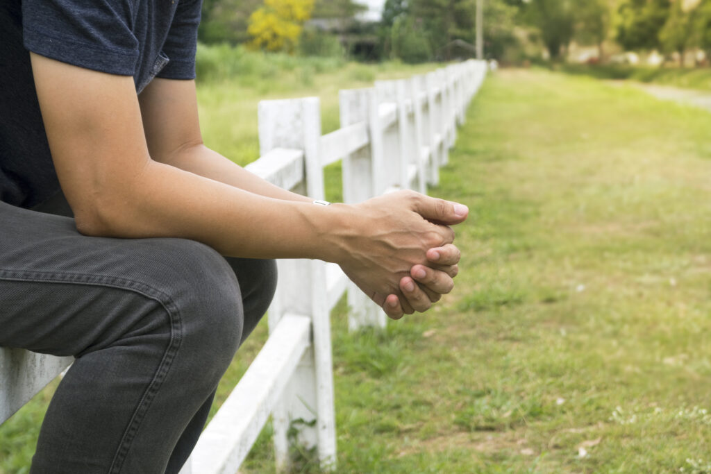Man sitting on long white fence. Image credit: iStock