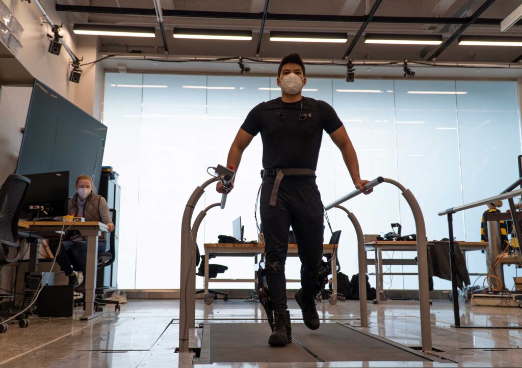 Leo Medrano, a PhD student in the Neurobionics Lab at the University of Michigan, tests out an ankle exoskeleton on a two-track treadmill. By allowing the user to directly manipulate the exoskeleton’s settings while testing it on a treadmill, preferences that are difficult to detect or measure, such as comfort, could be accounted for by the users themselves. Image credit: University of Michigan Robotics Institute
