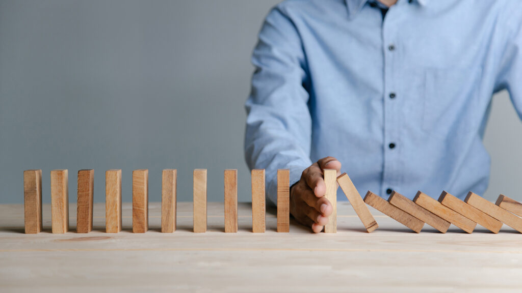 Businessman hand stopping the domino wooden effect. Image credit: iStock