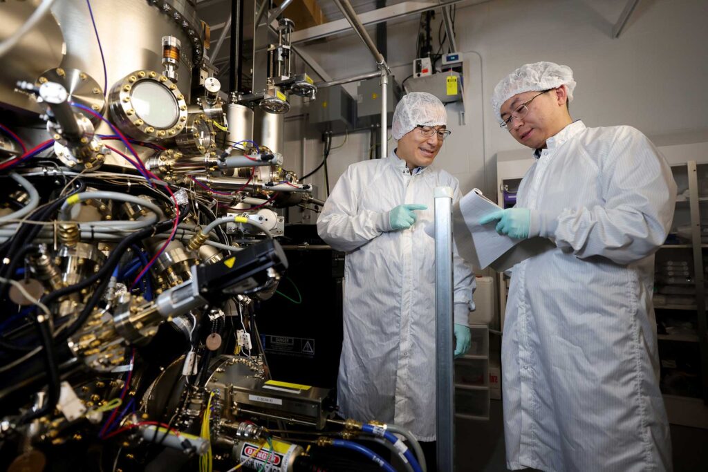 Zetian Mi, left, a professor of electrical engineering and computer science at U-M, and Ping Wang, a postdoctoral researcher in electrical engineering and computer science, discuss the growth process of monolayer hexagonal boron nitride on graphene substrate using an ultra high temperature molecular beam epitaxy system at their lab. This is the first method for producing high-quality, wafer-scale hexagonal boron nitride and the discovery could speed research into the next-generation computing and LED devices. Image credit: Brenda Ahearn