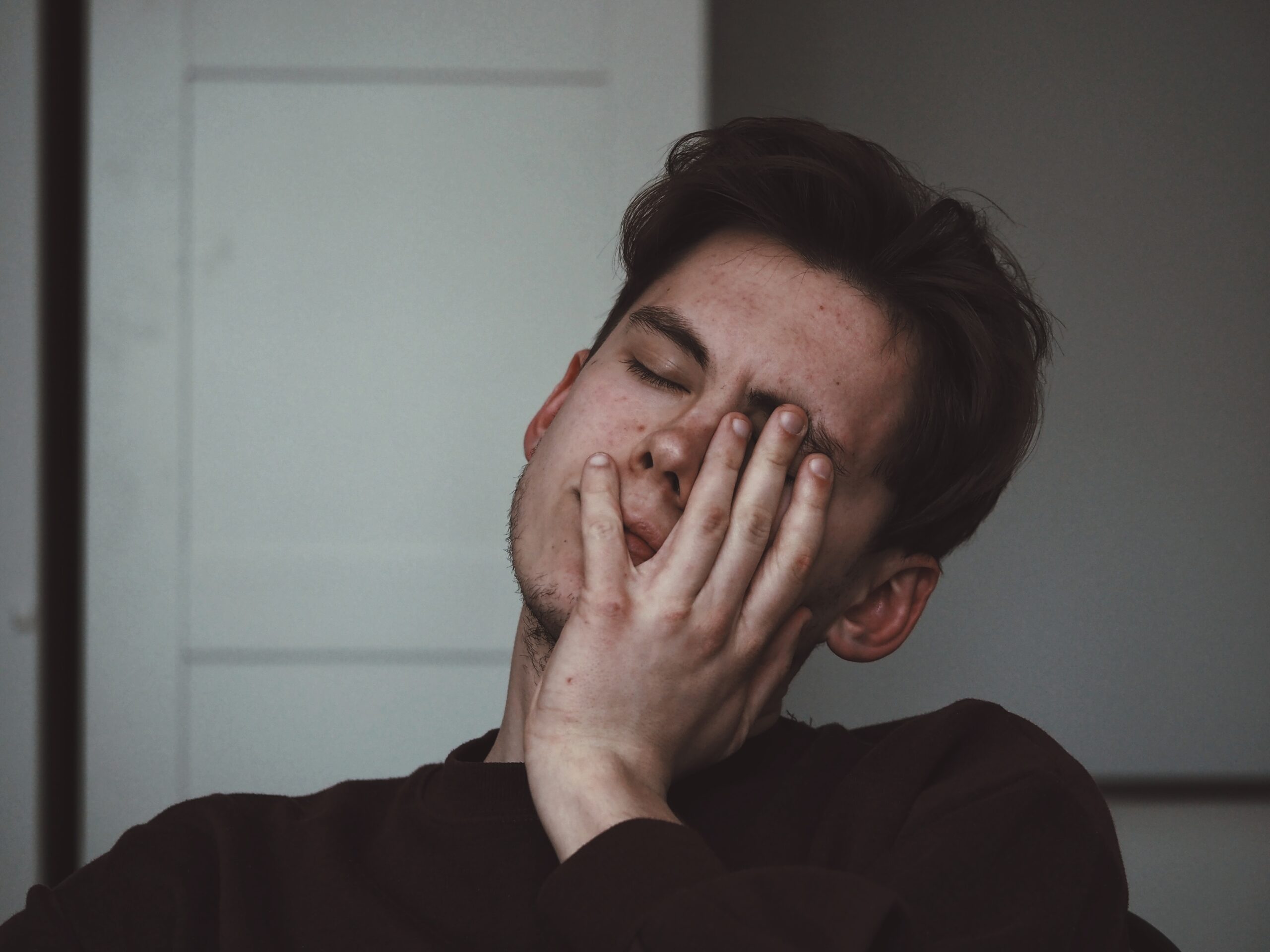 A tired man with his eyes closed and hand on his face. Image credit: Adrian Swancar, UnSplash.com