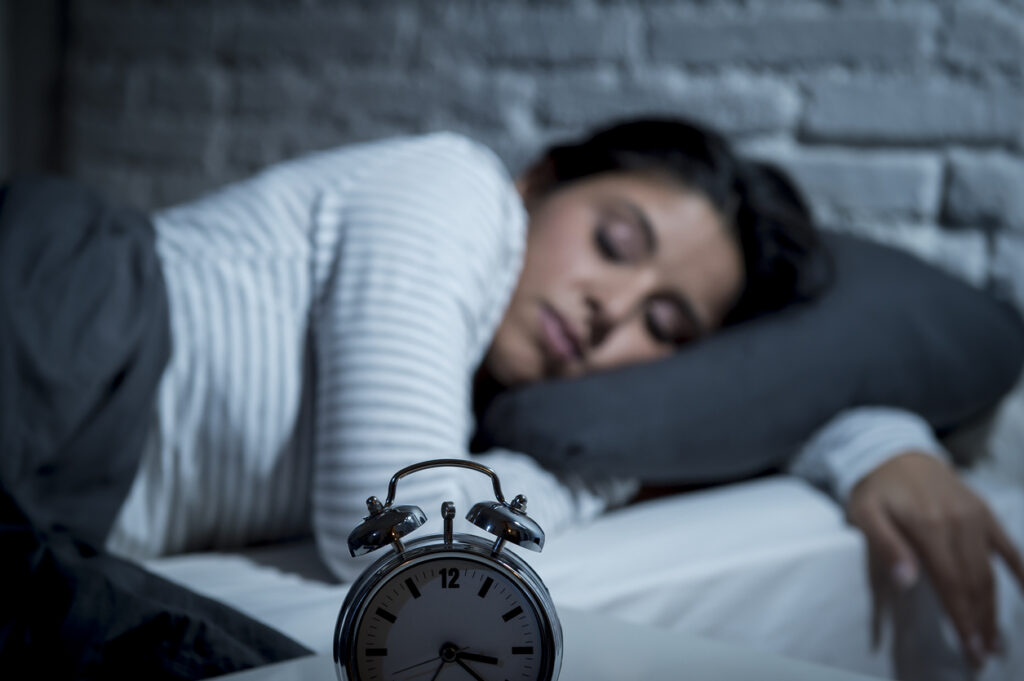 A sleeping woman with alarm clock in the foreground. Image credit: iStock