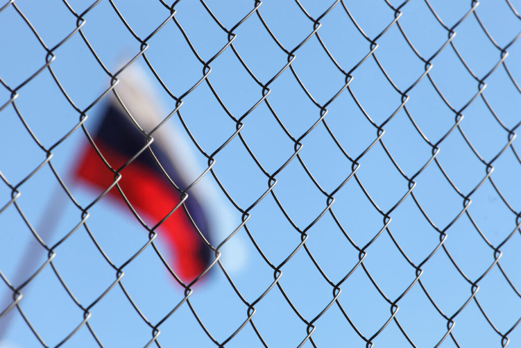 A fence of metal mesh behind which the Russian flag. Image credit: iStock