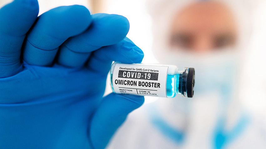 A gloved hand holding a vial labeled COVID-19 OMICRON BOOSTER. Image credit: Getty Images