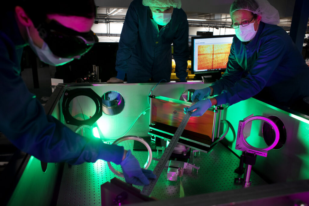 (From left) Laser engineer Lauren Weinberg, research scientist John Nees and research engineer Galina Kalinchenko pose for photos while working on the ZEUS laser at the NSF ZEUS laser facility in a Michigan Engineering lab. Image credit: Marcin Szczepanski, Michigan Engineering
