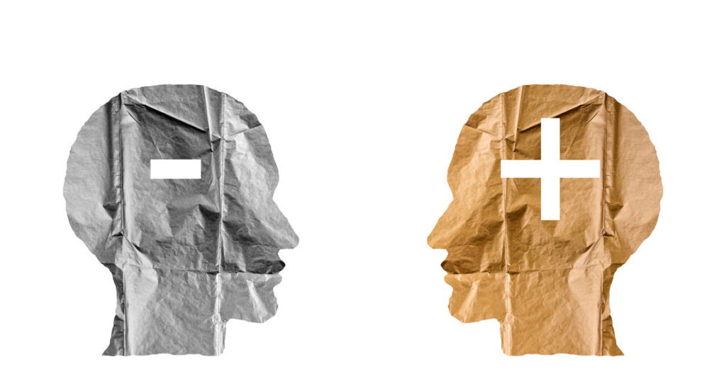 Crumpled paper shaped as a human heads and plus and minus signs. Positive and negative concept. Image credit: iStock