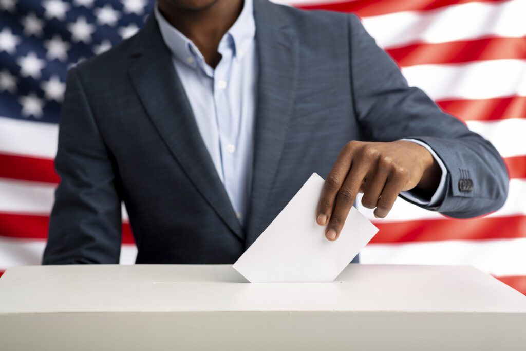 Black man holds envelope in hand above vote ballot. Image credit: iStock
