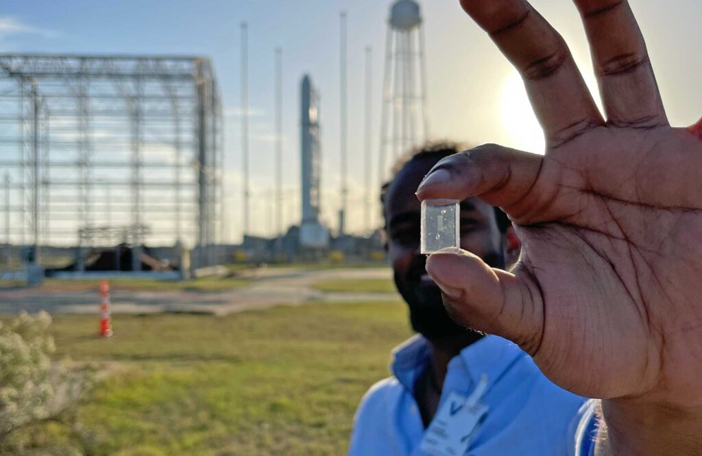 Nadab Wubshet, a doctoral student in mechanical engineering, stands near the launch site, holding up a microfluidic chip like those sent to the International Space Station Monday. Image credit: Samuel Chen