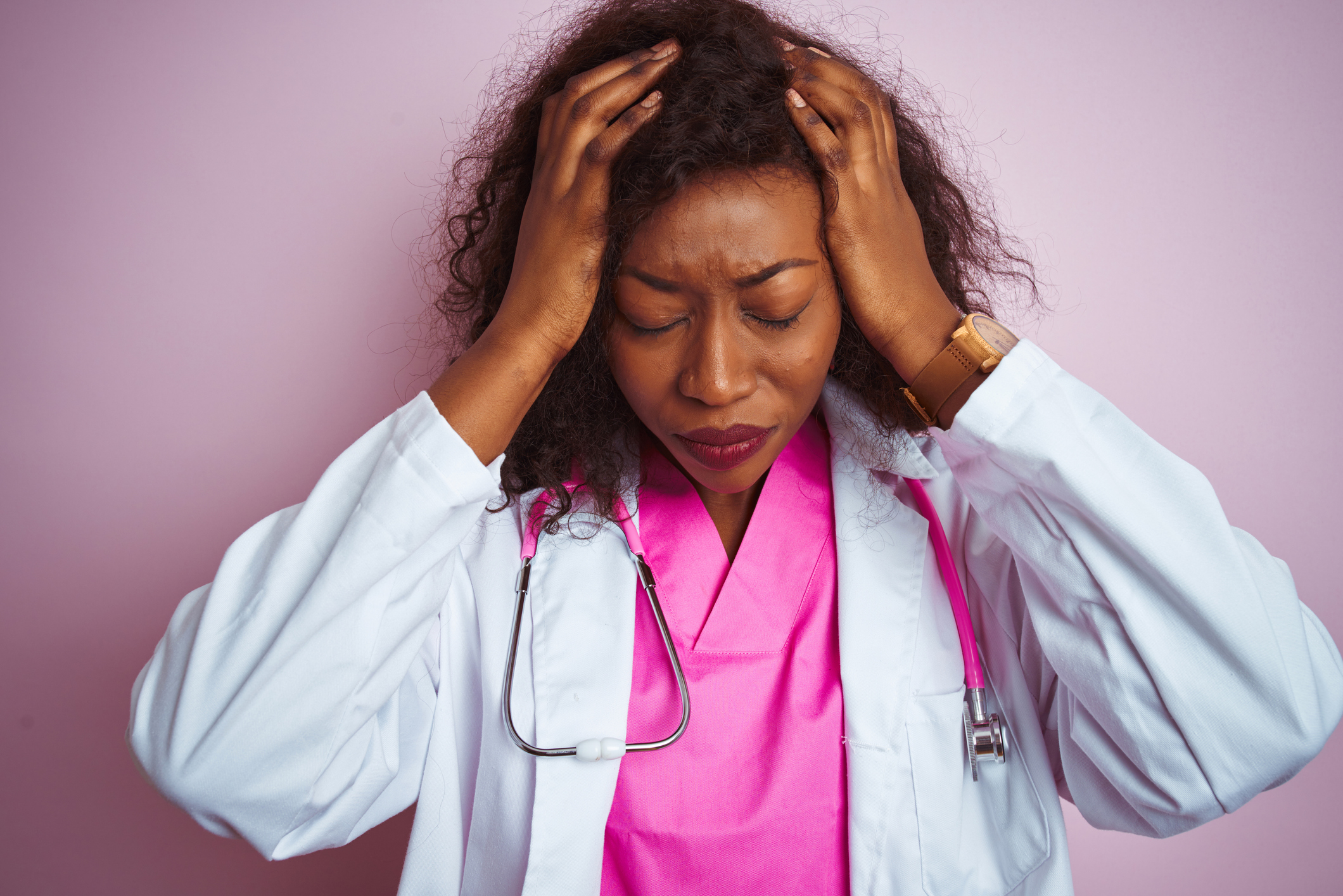 African american doctor woman wearing stethoscope over isolated pink background suffering from headache desperate and stressed because pain and migraine. Hands on head. Image credit: AaronAmat, iStock