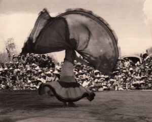 Bai-Chinese dancer Dong Lixin performs the Yi-style dance solo “Red Shawl” 红披毡 on an open-air stage. Contributor: Dong Lixin 董丽馨 (b. 1946)