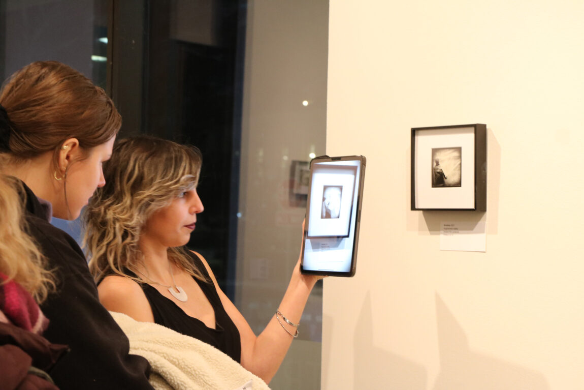 Artist Camila Magrane holds a tablet up to one of the pieces in her exhibition “Traces,” using augmented reality to unlock its animation. (Photo by Kiera Hollins)