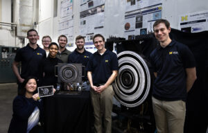 The team at the PEPL lab poses for a photo near the new Hall thruster and the older and bigger version of the thruster at the PEPL lab on the University of Michigan’s North Campus. From left are Ph.D students Leanne Su, Christopher Sercel, Thomas Marks, Madison Allen, Parker Roberts, Will Hurley andTate Gill. The second last on the right is Benjamin Jorns, U-M associate professor of aerospace engineering who led the new Hall thruster study. Image credit: Marcin Szczepanski/Lead Multimedia Storyteller, University of Michigan College of Engineering
