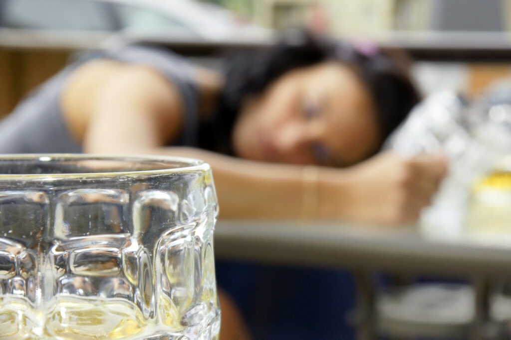 An empty glass in the foreground with a young woman passed on in the background. Image credit: iStock