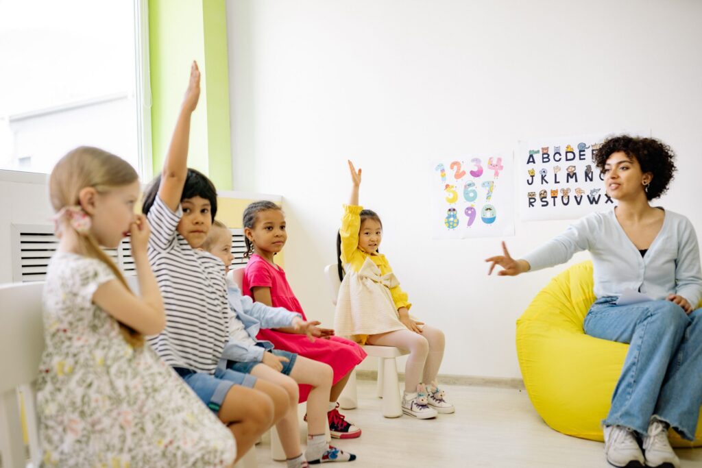 Teacher giving lesson and children raising their hands. Image credit: Yan Krukau, Pexels