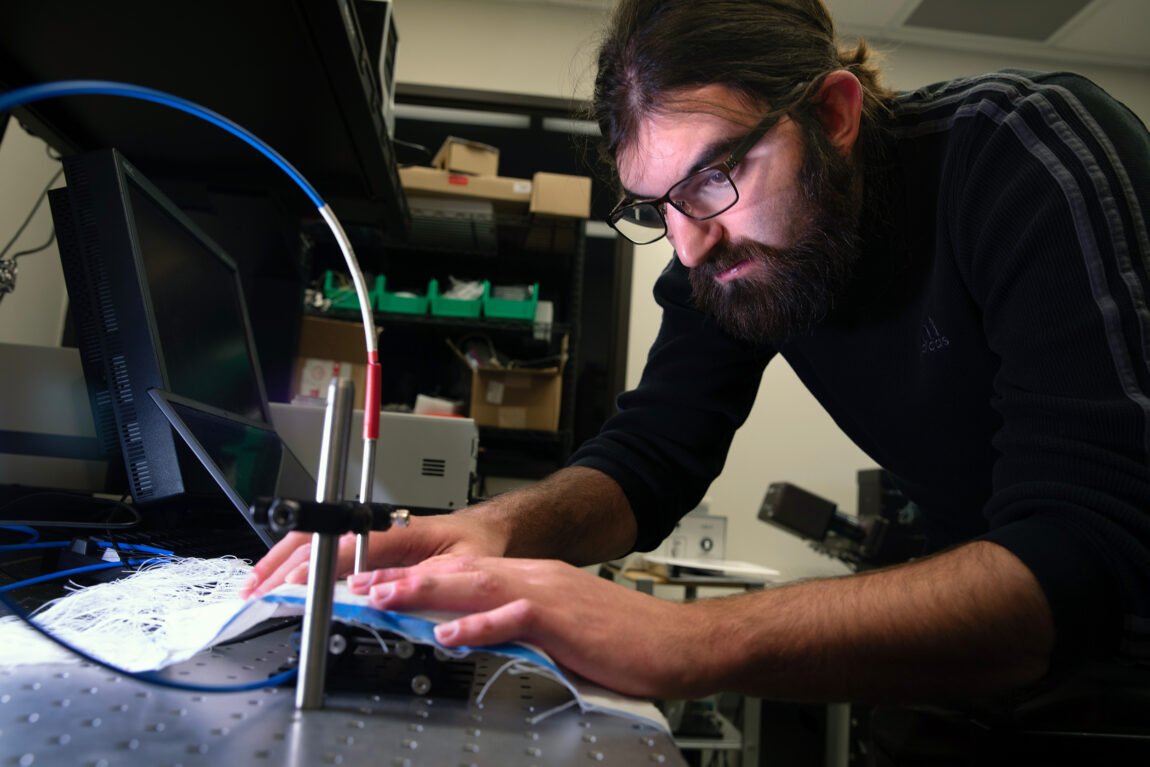 Brian Iezzi, a postdoctoral researcher, scans and measures the photonic fibers in the fabric he developed. (Photo by Marcin Szczepanski, College of Engineering)