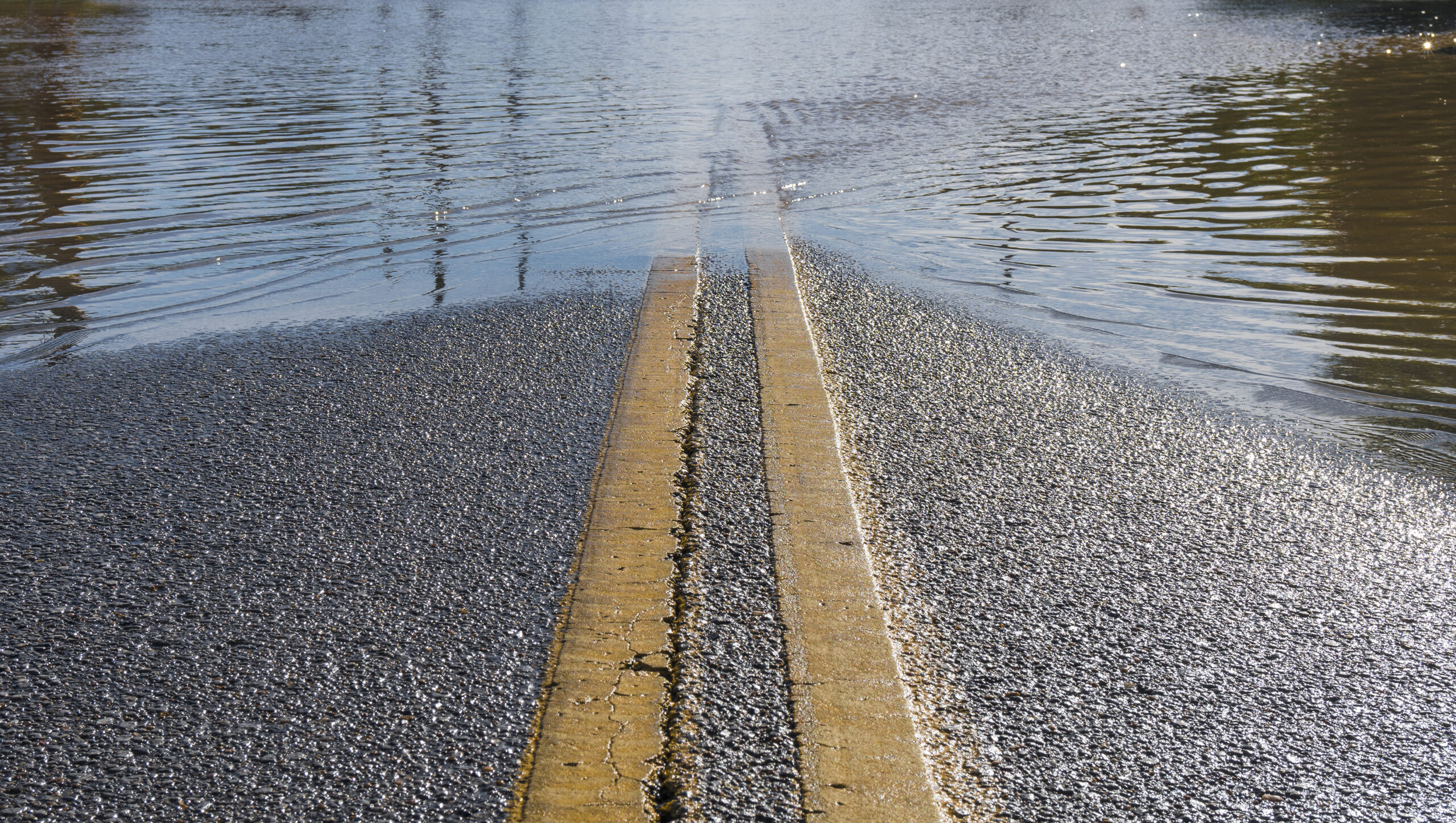 Road with yellow center stripe leading into flooded area on the horizon.