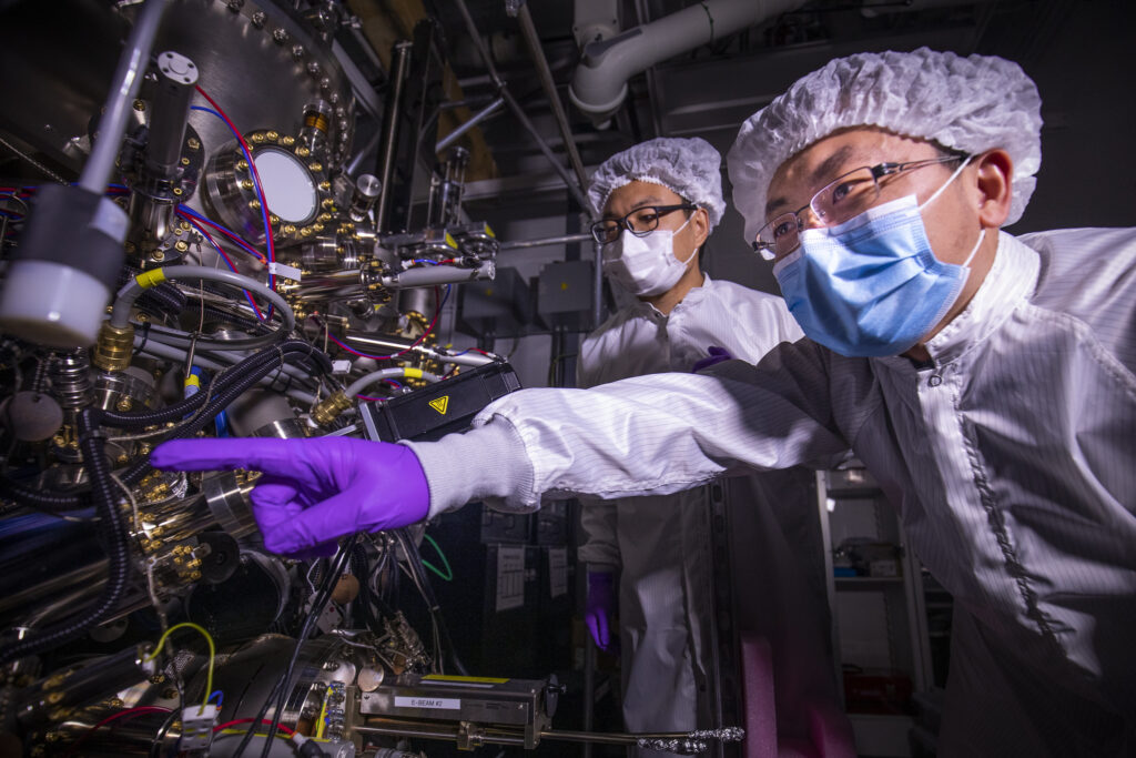 Research scientists Ding Wang (left) and Ping Wang (right) discuss the growth behavior of the ferroelectric semiconductor deposited using the molecular beam epitaxy system that is visible on the left. The semiconductor could make computing more efficient, enhance AI and enable quantum computing. Image credit: Robert Coelius.