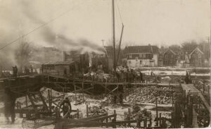 1917: Crews begin construction on the Michigan Union. Sepia photography of rubble, workers, smoke.