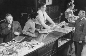 A black & white image of male staffers working at the front desk of the Michigan Union, selling newspapers and other sundries.