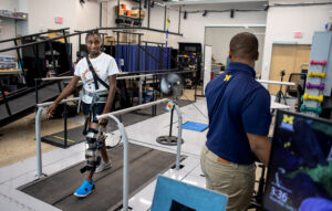 Research subject Therese Nkeng laughs while struggling to use her body to keep balance when the mechanism on her knee forces her knee joint to give up while walking on a treadmill. Image credit: Marcin Szczepanski, Michigan Engineering
