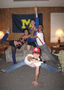 Burton and friends pose in an apartment with a large blue flag featuring a block M.