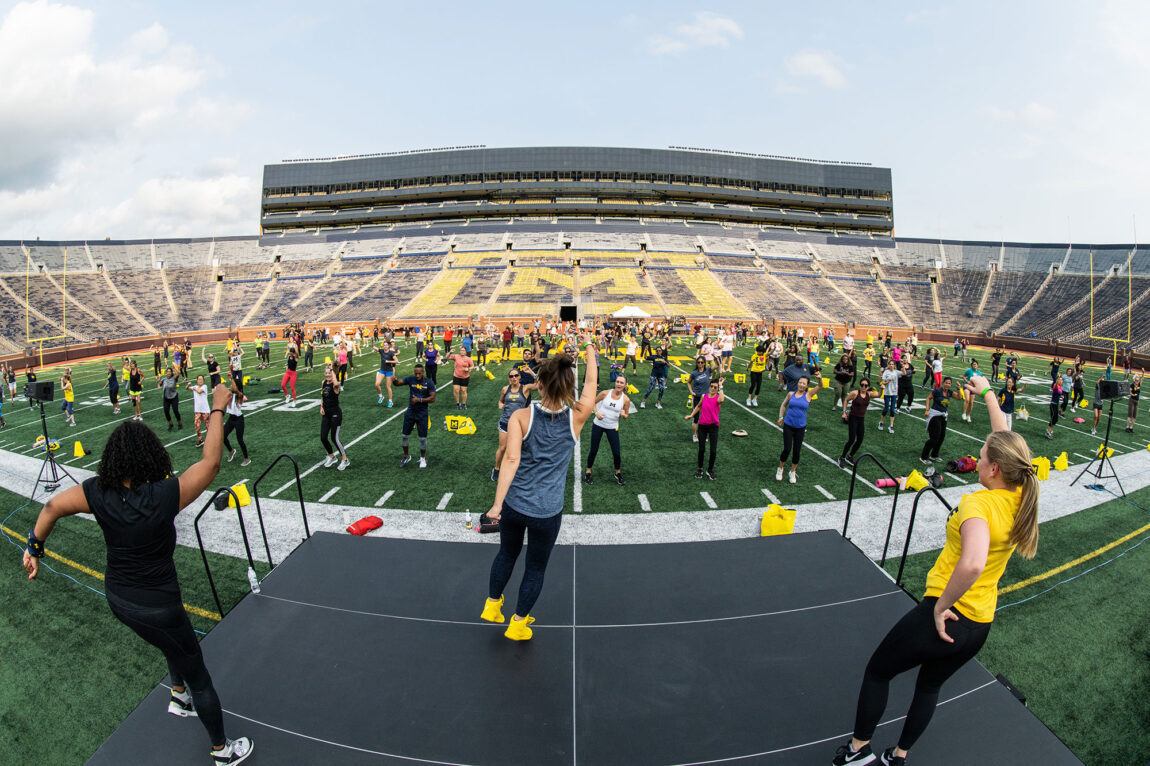 Photo of exercise instructors leading exercises for people on the Michigan Stadium field