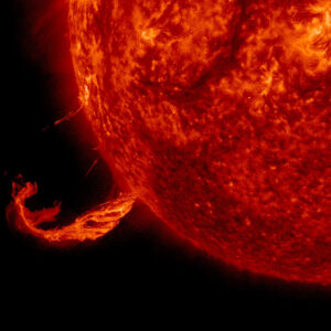 The sun appears as a fiery red sphere that encompasses the right two-thirds of the image. A column of red fire protrudes from the sun’s surface toward the bottom left corner of the image.