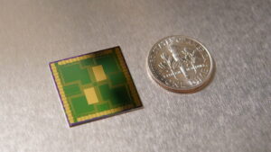 The multi-electrode array is a lime-green square about the size of a dime. It has small, gold squares and rectangles around its border with two larger golden rectangles in the middle. Pathways of thin gold lines cross between the gold in the middle and the gold at the edges.