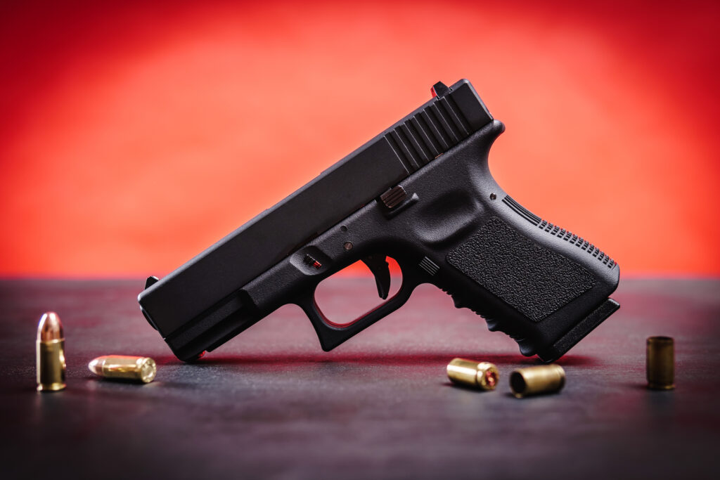 A pistol on a table with bullets against a red background. Image credit: iStock