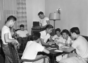 Young Japanese men play cards. Black & white. One wears a Michigan t-shirt.