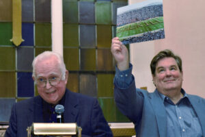 Two men stand at the podium for a ceremony. Both are caucasian. It's Dick Gaskill and Mark Gaskill celebrating Dick's induction to the Livonia Hall of Fame.