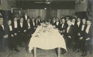 Football players in formal attire sit at a dining table in 1905.