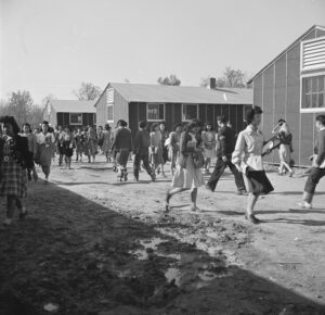 Black & white image of Japanese high school students changing classes amid the barracks at Rowher detention camp.