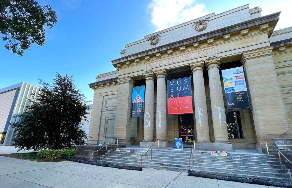 Alumni Memorial Hall at the U-M Museum of Art pictured at dusk with lights on and 3 banners between columns. Image credit Scott Soderberg, Michigan Photography