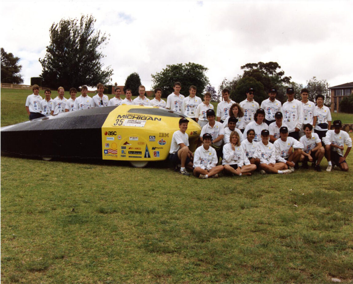 A photo of a solar-powered car and college students