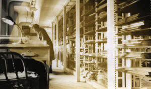 A sepia image of a woman working in a library in the early 20th century.