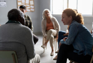 A group of people are seated in a circle listening to one person speak.