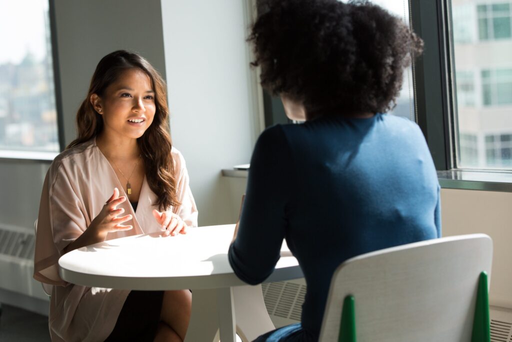 Two women speak across a table. Image credit: wocintechchat, Unsplash