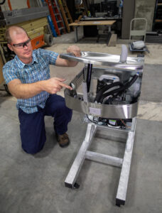 Justin Roelofs, Engineering Technician at the Civil and Environmental Engineering Department at the College of Engineering points to the demonstration water fountain that prof. Nancy Love and her team will use to demonstrate to public school students in Flint how the water filtration system works. Justin Roelofs built a metal base of the water fountain. Image credit: Marcin Szczepanski, Michigan Engineering