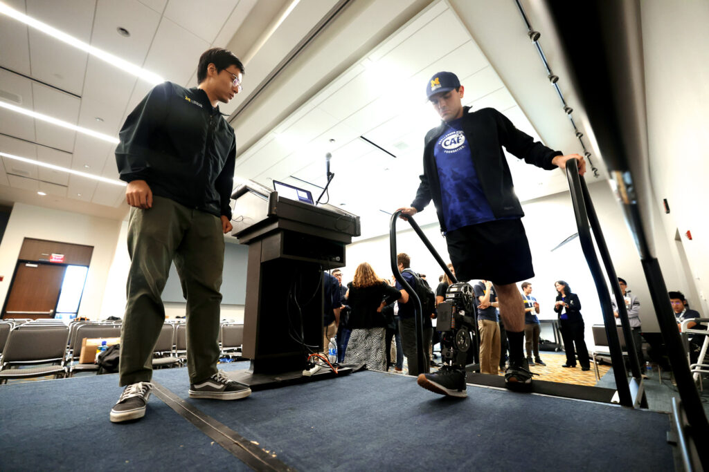Andrew Seelhoff, left, a first-year PhD student in mechanical engineering at the University of Michigan, demonstrates the robotic prosthetic designed by Robert Gregg’s Locomotor Control Systems Laboratory, at IROS 2023 in October. Image credit: Brenda Ahearn, Michigan Engineering
