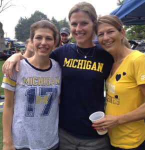 Three caucasian women dressed in Michigan gear are tailgating