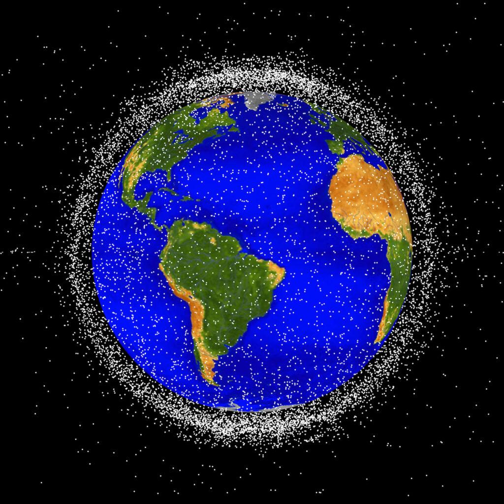 The space junk appears as many small white points surrounding Earth, which has bright blue oceans and green and brown continents. The space junk is thick enough to form a cloud that obscures most of the black background when viewed from the edges around Earth.